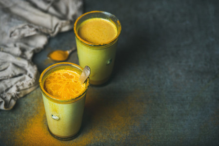 Golden milk with turmeric powder in glasses over grunge background