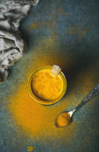 Golden milk with turmeric powder in glass over dark background