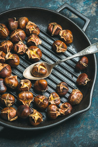 Close up of roasted chestnuts and spoon in grilling pan