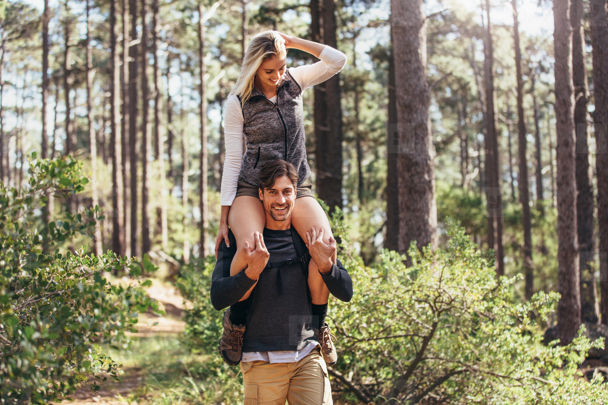 Woman riding piggyback on man during hiking in forest. 
