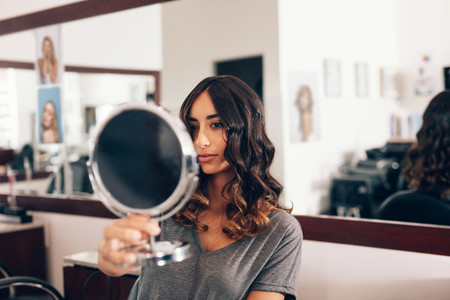 woman in salon with curled hairstyle looking herself in mirror