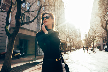 Stylish female walking on city street and talking on phone