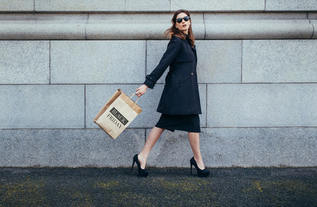 Stylish female shopper walking with shopping bag