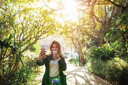 Woman clicking a selfie in park holding a coffee glass