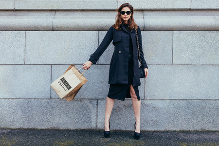 Stylish woman against wall with shopping bags