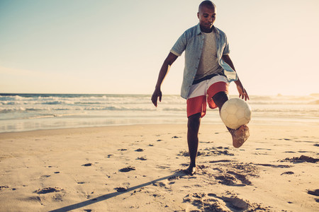 African man playing with soccer ball at beach