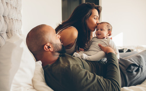 Parents with their newborn baby boy on bed