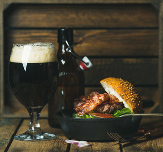 Beef burger with crispy bacon and glass of dark beer