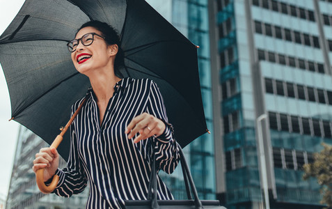 Young smiling businesswoman with umbrella outdoors