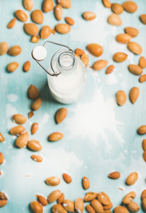 Almond milk in bottle and fresh nuts over blue background