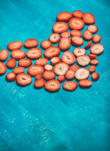 Heart of fresh strawberries over bright blue painted background