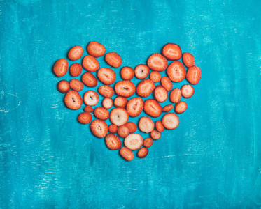 Pieces of fresh strawberry placed in heart shape blue background