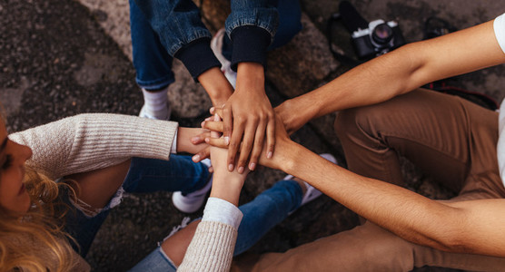 Group of friends sitting together stacking their hands on one an