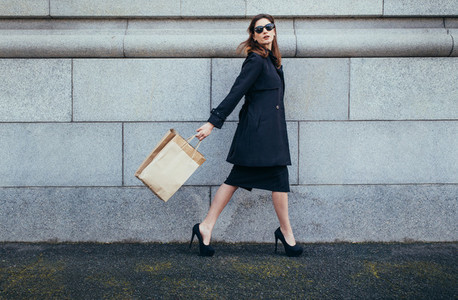 Stylish female shopper walking with shopping bag