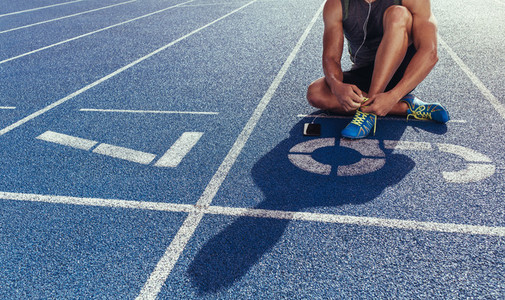 Sprinter tying shoe lace sitting on running track