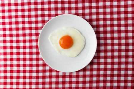 Fried egg overhead on plate on breakfast tablecloth