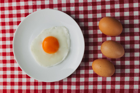 Fried eggs overhead on plate on breakfast tablecloth