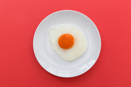 Fried egg and yoke overhead on plate and red background