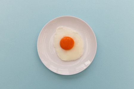 Fried egg and yoke overhead on plate and blue background