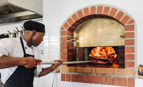 Chef baking pizza in wood fired oven