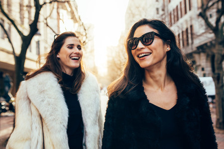 Female friends in warm clothes walking on the city street