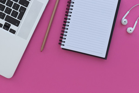 Notebook laptop computer and earphones on bright pink background