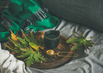Black mug of tea with sieve and leaves on tray