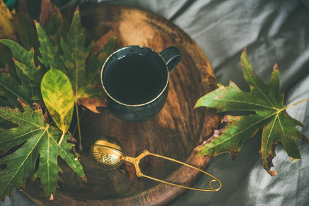 Mug of tea with sieve and colofrul autumn leaves