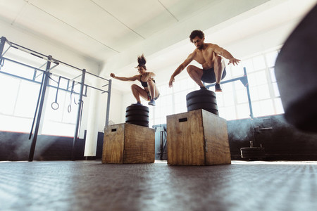 Healthy man and woman box jumping at gym