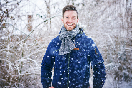 Young handsome man in snowfall smiling cheerfully
