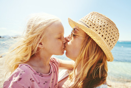 Young mother and her daughter kissing at the beach