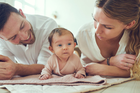 Smiling young parents lying with their baby girl at home