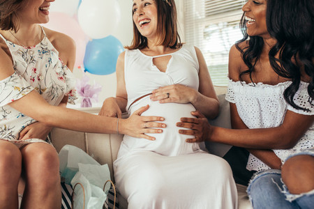 Smiling friends touching tummy of pregnant woman