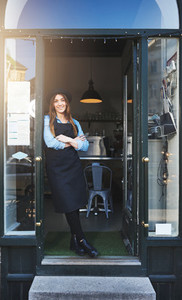 Cheerful barista leaning against doorway in cafe