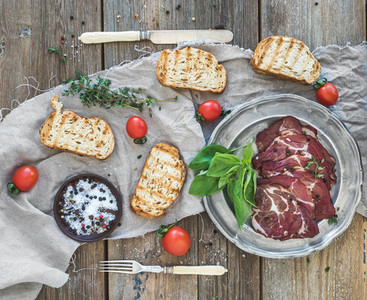 Smoked meat in vintage silver plate with fresh basil cherry tomatoes and bread slices over rustic wood