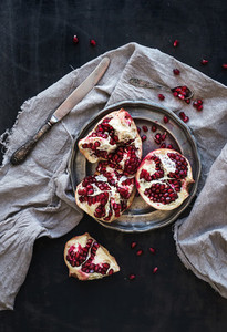 Red ripe peeled pomegranate on rustic metal plate and beige kitchen towel