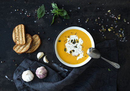 Pumpkin soup with cream seeds bread and fresh basil on grunge black background
