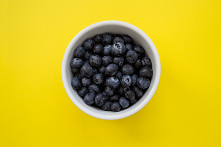 Bowl of blueberries on yellow background