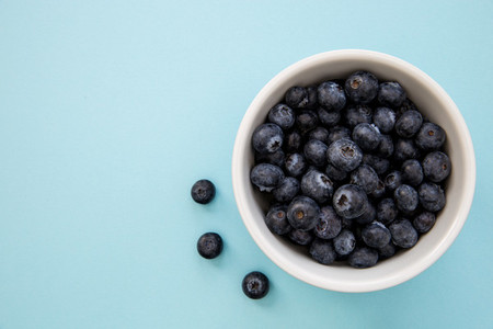 Bowl of blueberries on blue background with copy space