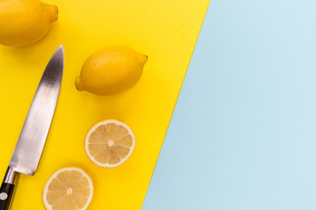 Sliced lemons and knife on bright yellow and blue background