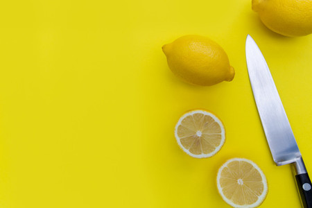 Sliced lemon fruits and knife on bright yellow background with c