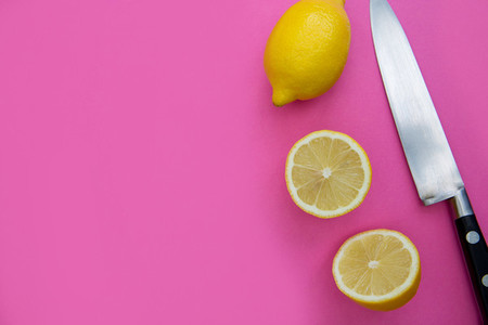 Sliced lemons and knife on bright pink background with copy spac