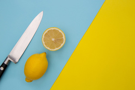 Sliced lemons and knife on minimal yellow and blue background
