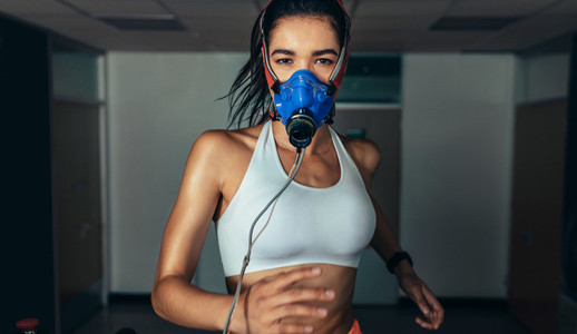 Sportswoman with mask running on treadmill in gym