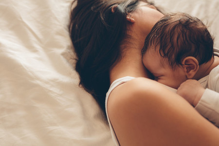 Newborn baby boy sleeping with his mother on bed