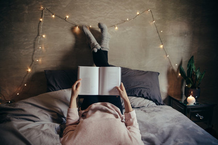 Woman lying on bed and reading book