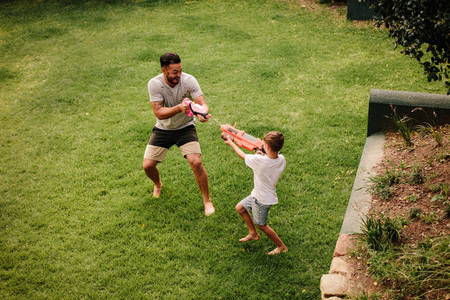 Father and son playing water gun fight outdoors