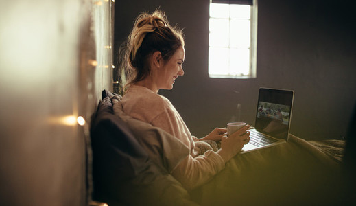 Woman on bed using laptop and having coffee