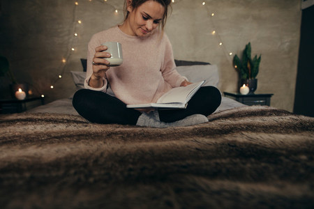 Relaxed woman on bed reading book with coffee