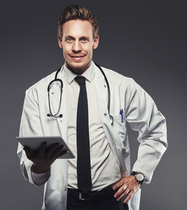 Smiling young doctor with a tablet against a grey background